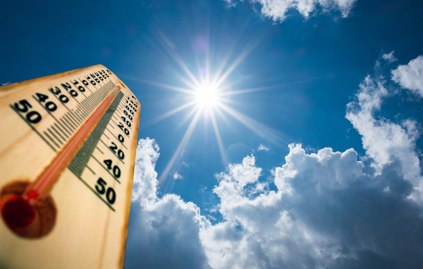 Holzthermometer zeigt heiße Temperaturen unter einer strahlenden Sonne mit blauem Himmel und Wolken.